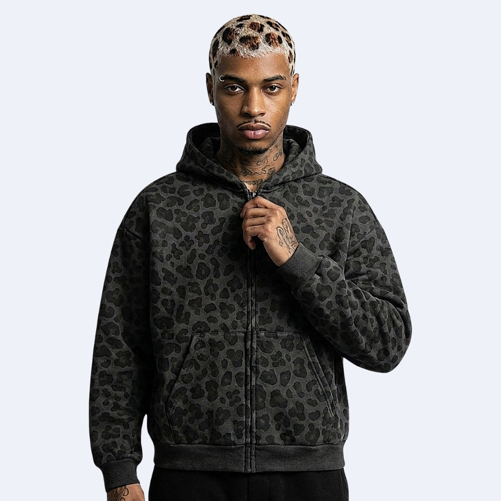 Black. KRUX Feral black leopard-print zip-up hoodie on a male model, front view holding the zipper