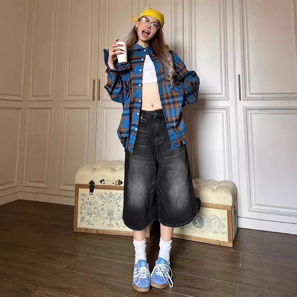 Person wearing a blue plaid shirt, black pants, and blue sneakers in a room with wooden floors and white walls.