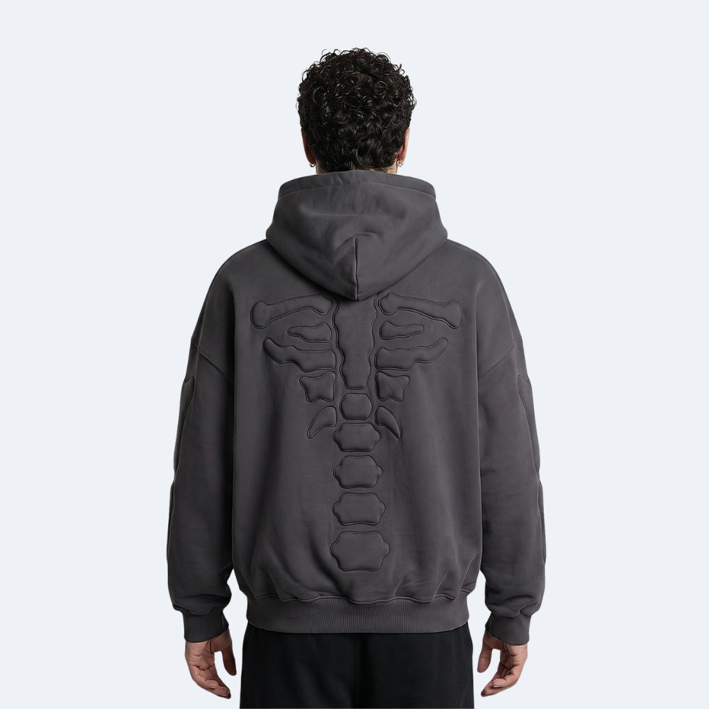 Black. A man viewed from behind wearing a dark gray oversized hoodie with a large raised rib cage design on the back, paired with black pants.