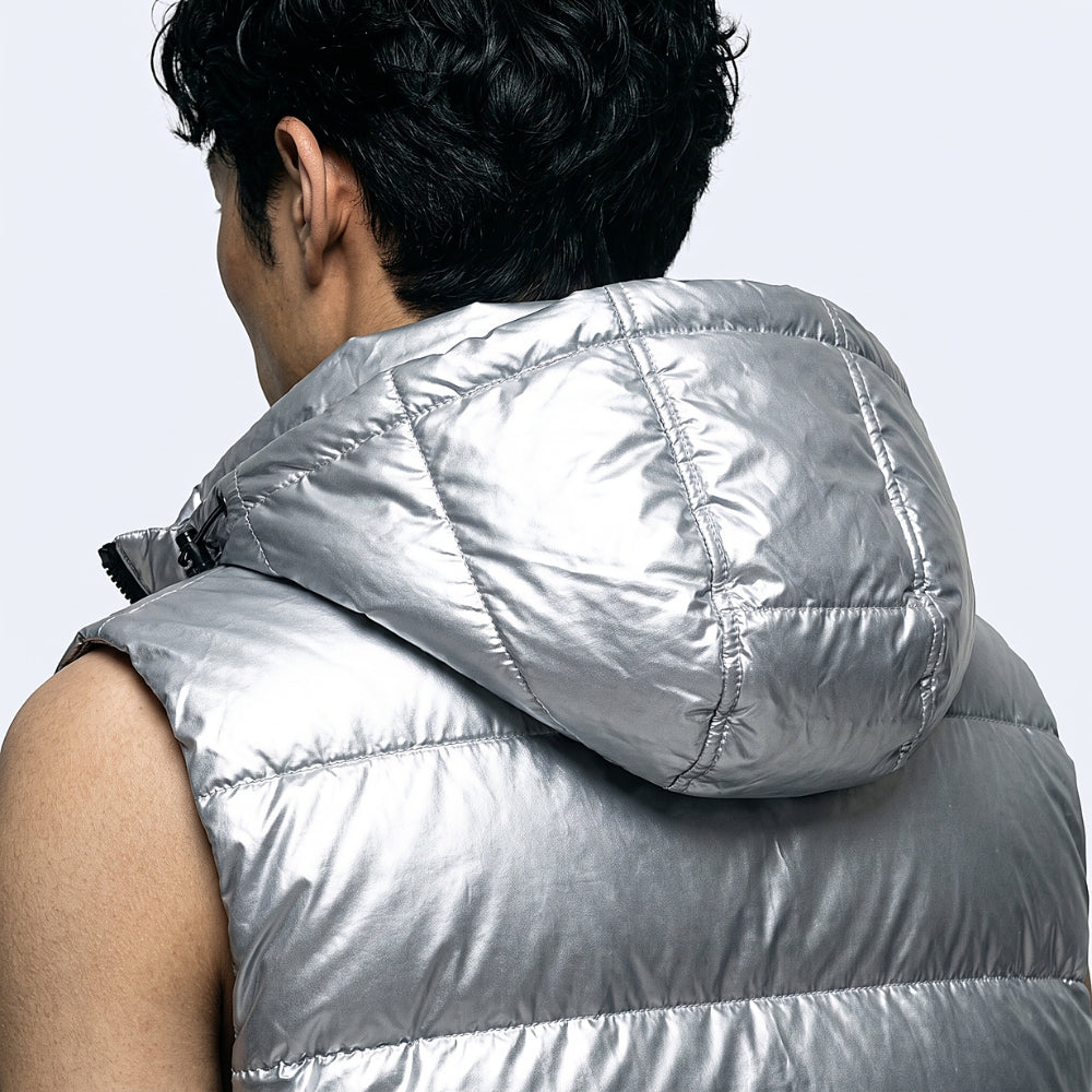 A close-up back view of a person wearing a shiny silver sleeveless puffer vest with a padded hood, against a light gray studio background.