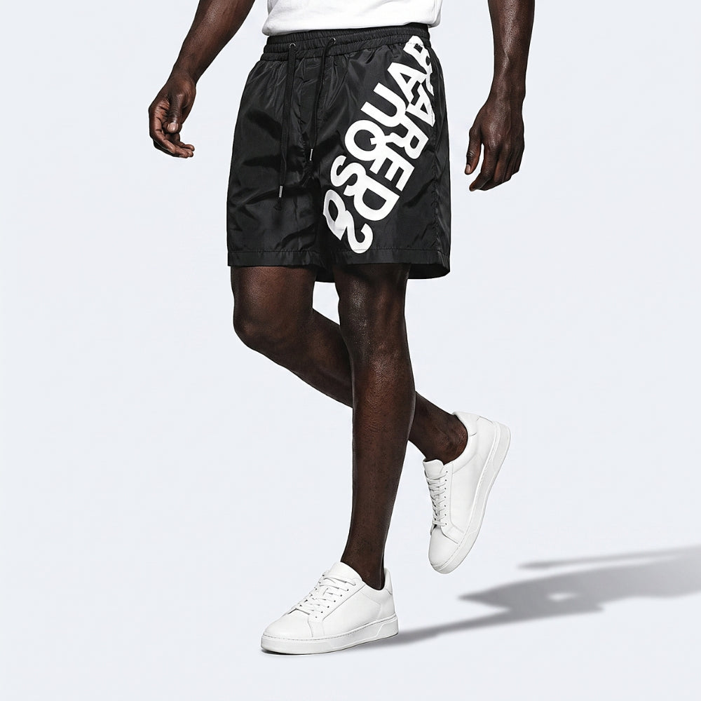Black. A model wearing black shorts with a large white logo printed diagonally on the side, paired with white sneakers.