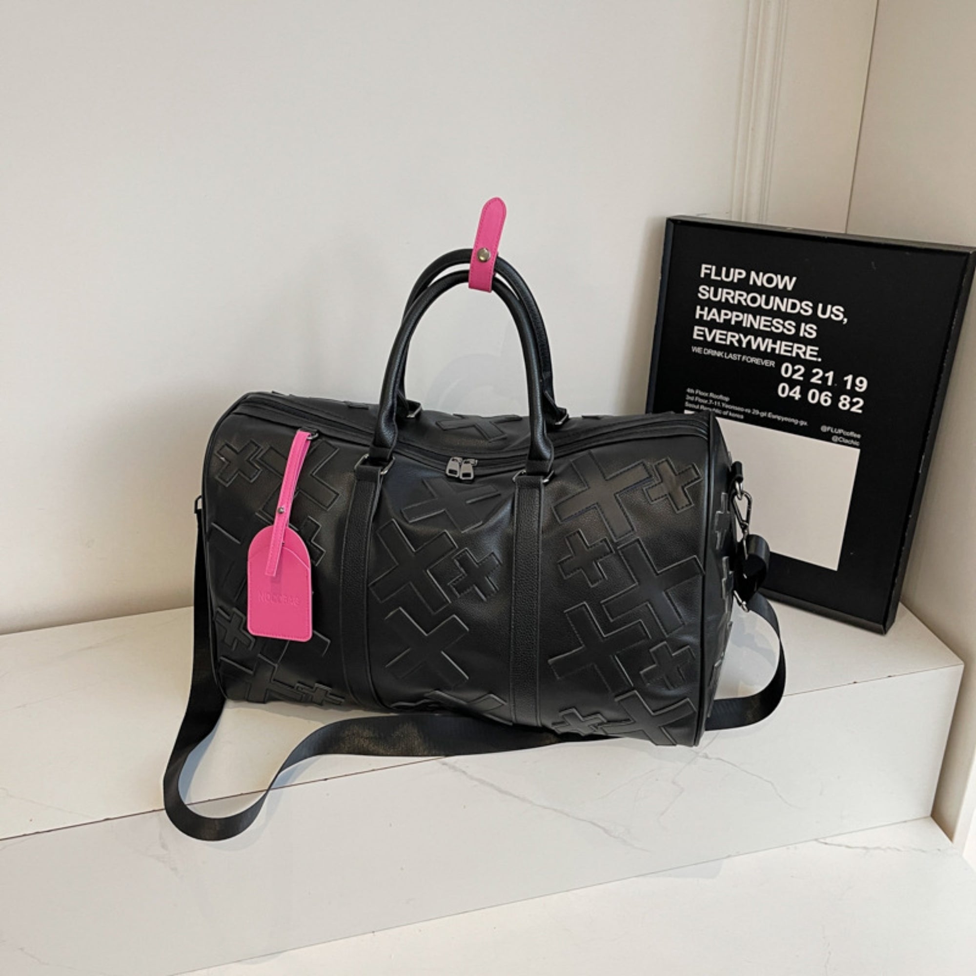 Black textured duffel bag with pink tags on a white surface