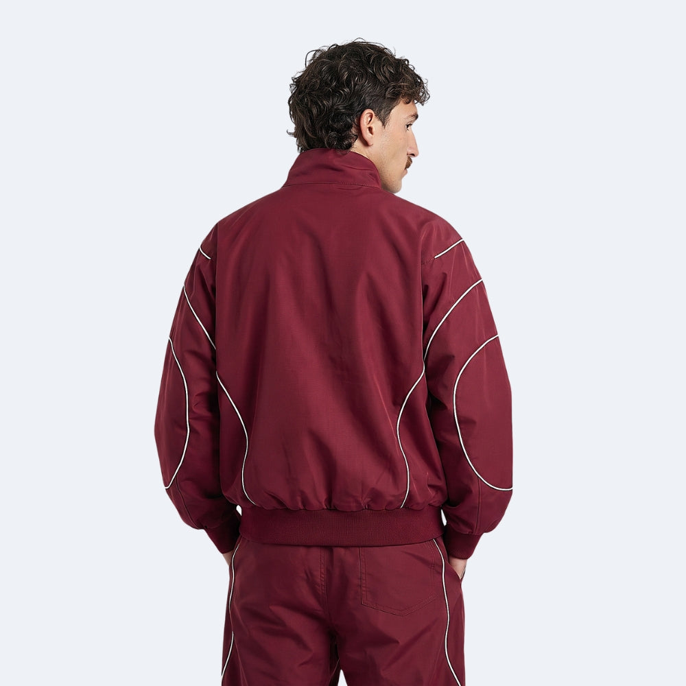 A man shown from the back wearing a maroon athletic jacket and matching pants with white contrast piping, against a light gray studio background.