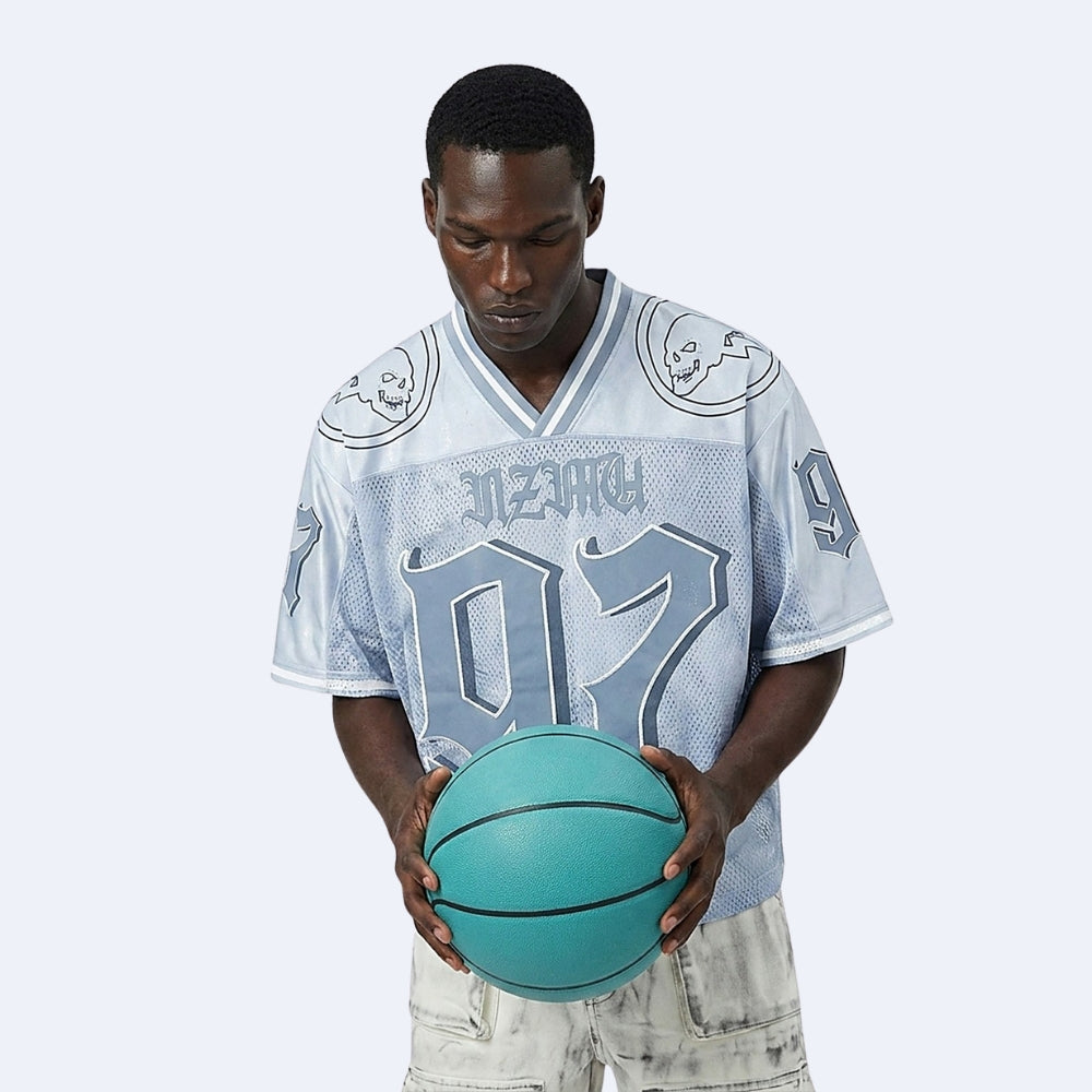 A man wearing a light blue and white graphic basketball jersey with the number 07 and holding a teal basketball, set against a solid light gray background.