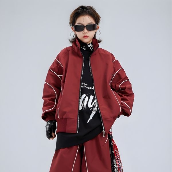 Person wearing a red jacket and black outfit with sunglasses on a gray background