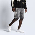 A model wearing gray denim shorts with a large white skeleton print down the side, styled with a black fleece zip-up hoodie and white sneakers against a light gray studio background.