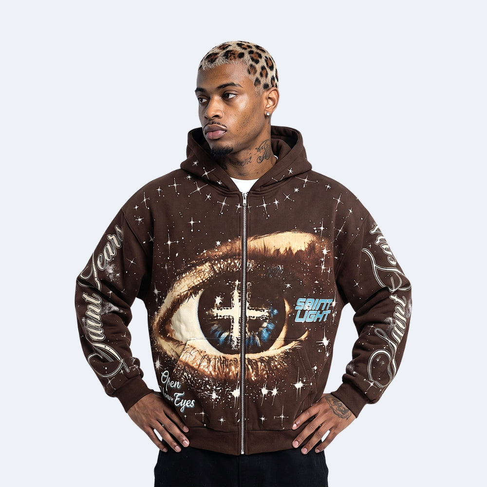 Brown. A man wearing a brown zip-up hoodie with a large cosmic eye graphic on the front, featuring text on the chest and sleeves.
