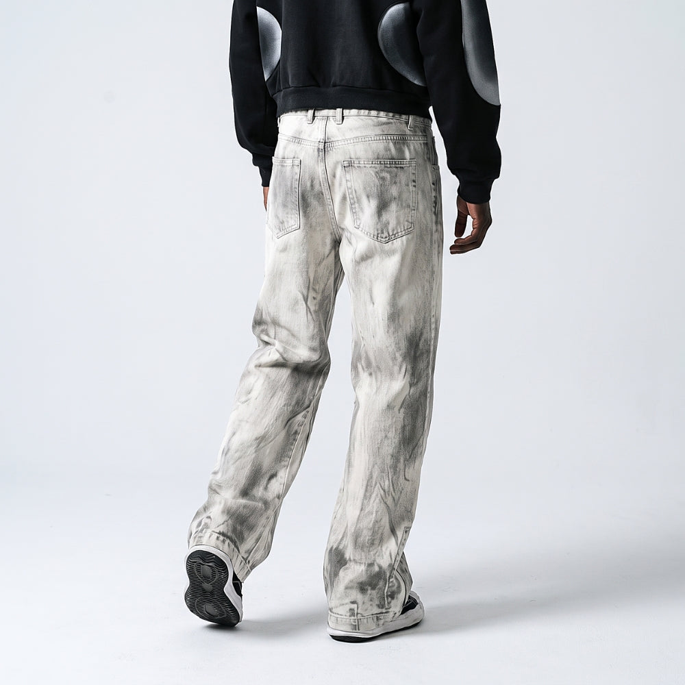 A person shown from the back wearing washed light gray denim jeans with a black sweatshirt and black sneakers, photographed against a clean light gray studio background.