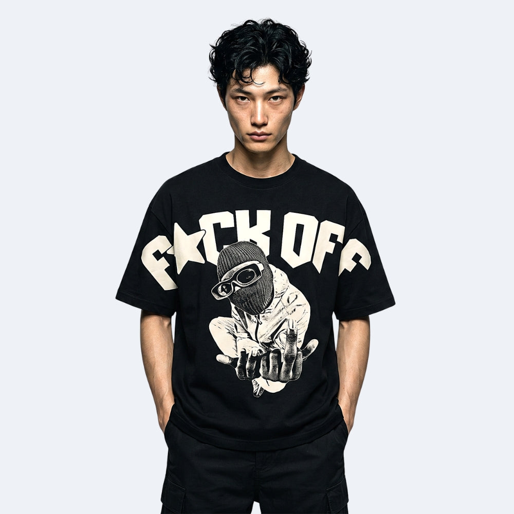 A man wearing a black graphic t-shirt with a large cream-colored 'F*CK OFF' text and a biker-style illustration on the front, set against a plain light gray background.