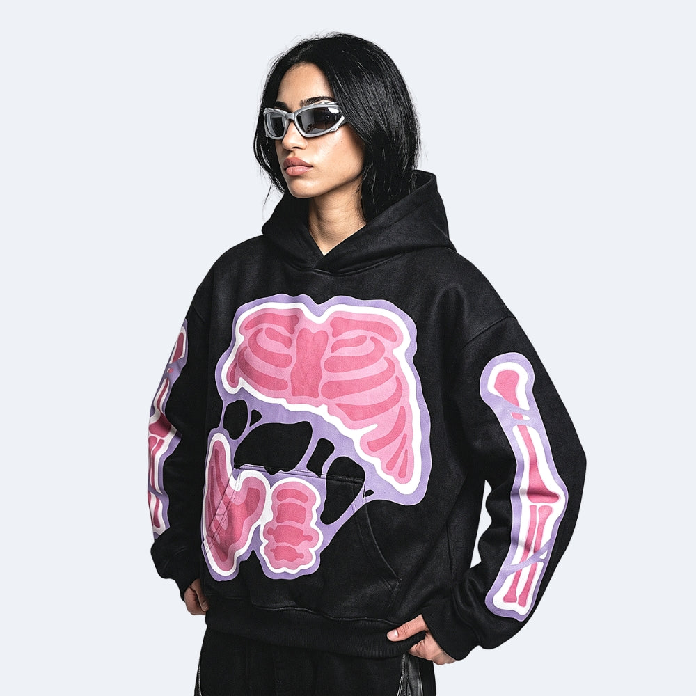 A model wearing a black hoodie with a large pink and purple anatomical skeleton graphic on the front and sleeves, styled with silver sunglasses against a light gray background.