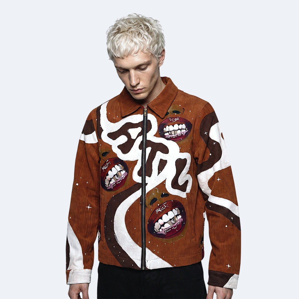 A model with platinum blonde hair wearing a brown corduroy jacket with a unique graphic print featuring white calligraphic shapes, dark brown swirls, and red-and-white mouth illustrations, set against a light gray background.