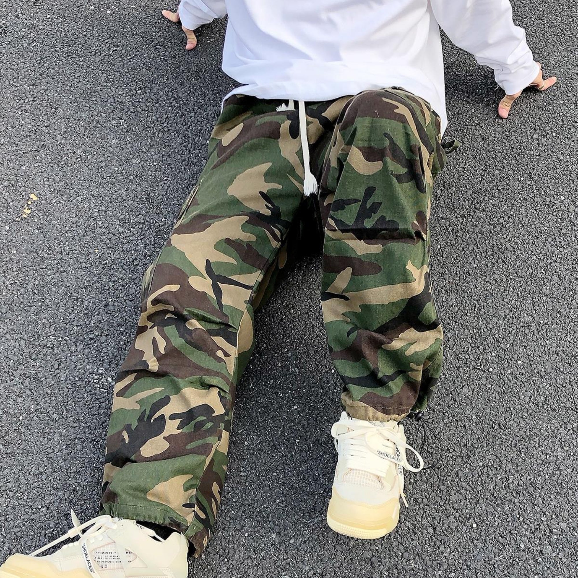 Person wearing camouflage pants and white sneakers on a gray pavement.