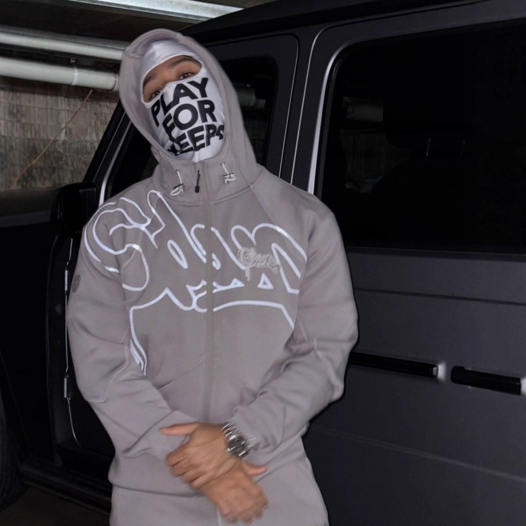 Person wearing a gray hoodie with white graphics and text, standing next to a black vehicle.
