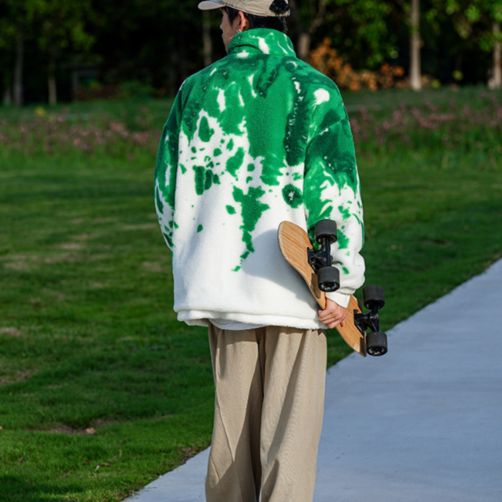 Person wearing a green and white jacket holding a skateboard on a path with grass and trees in the background