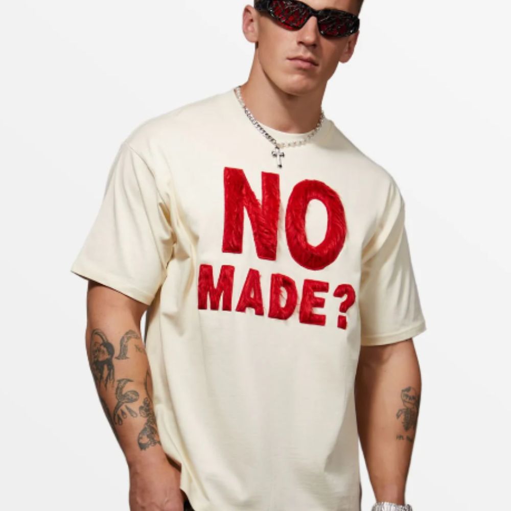 Person wearing a white t-shirt with red text 'NO MADE?' on a plain background
