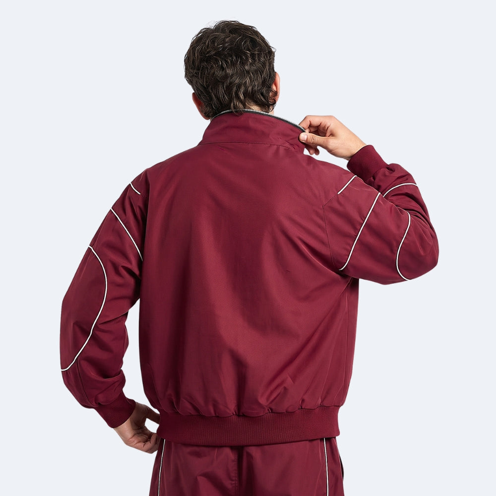 A man viewed from behind wearing a maroon track jacket with white piping details on the sleeves, against a light gray background.