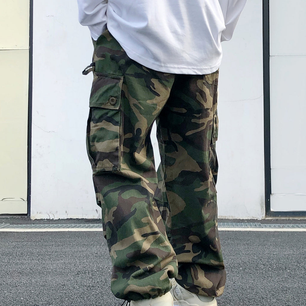 Person wearing camouflage cargo pants with a white shirt in an urban setting.