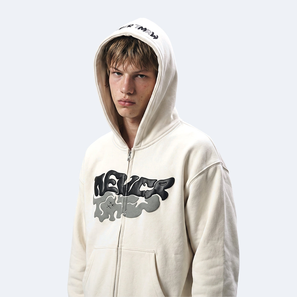 White. A young man wearing a cream-colored zip-up hoodie with a large black and gray graphic on the front and a small black graphic on the hood.