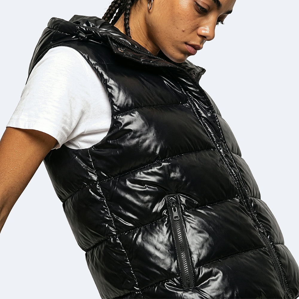 A close-up of a model wearing a shiny black puffer vest over a white t-shirt, shown from the side against a light gray background.