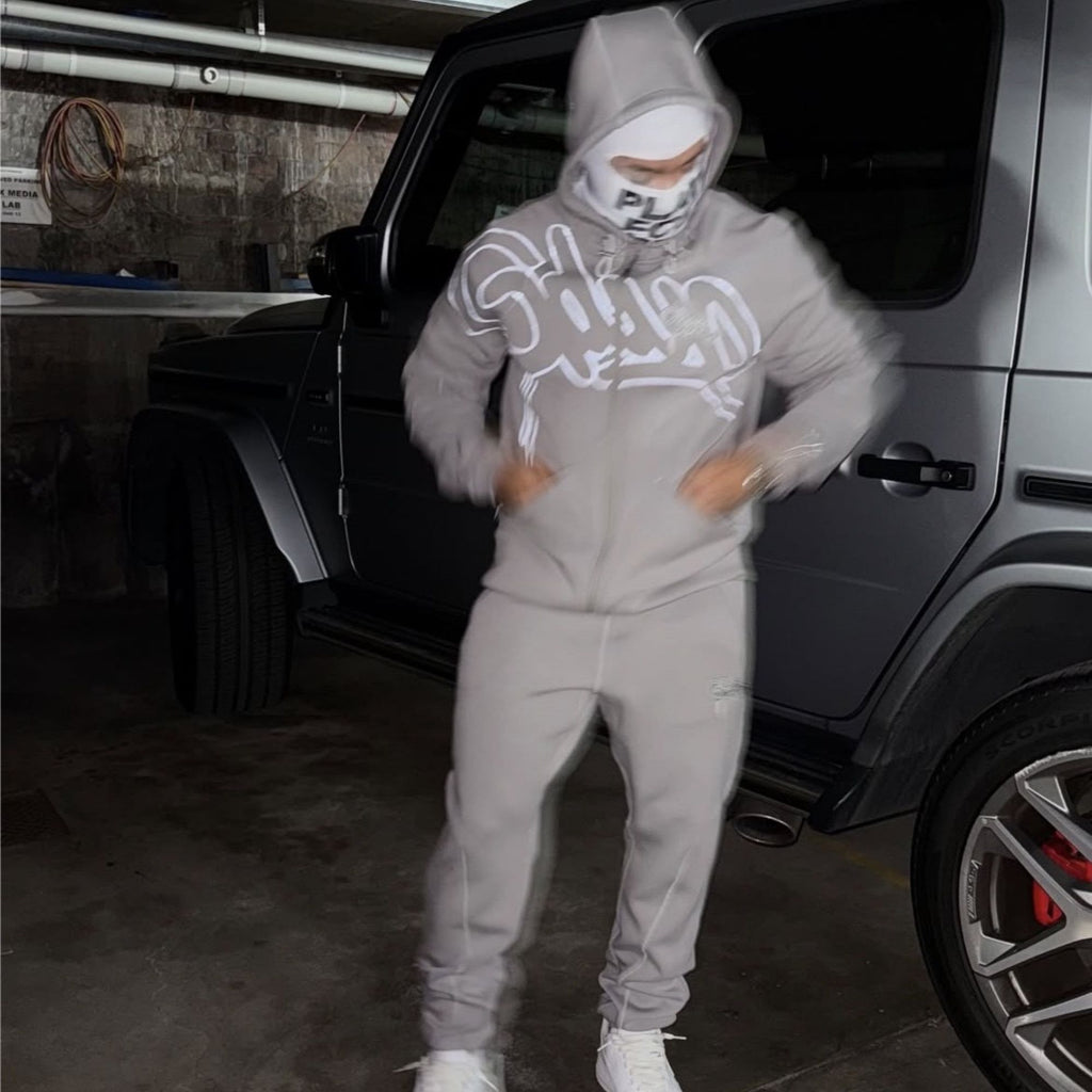 Person wearing a gray hoodie and pants in front of a car