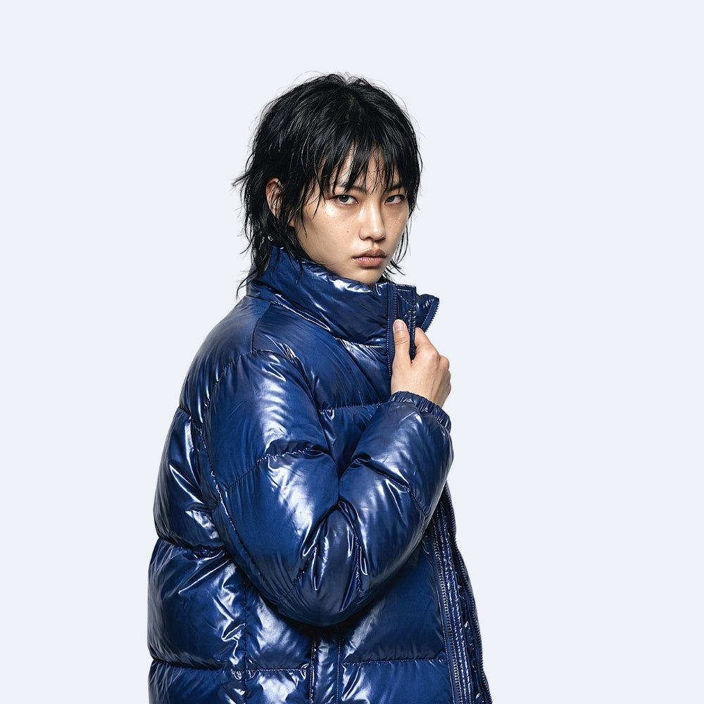 Navy. A model wearing a shiny, glossy royal blue puffer jacket with a high collar.