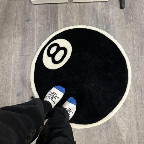 Round black doormat with number 8 design on a wooden floor.