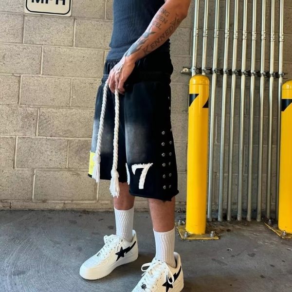 Person wearing black shorts with number 7, white sneakers, and holding a rope against a wall.