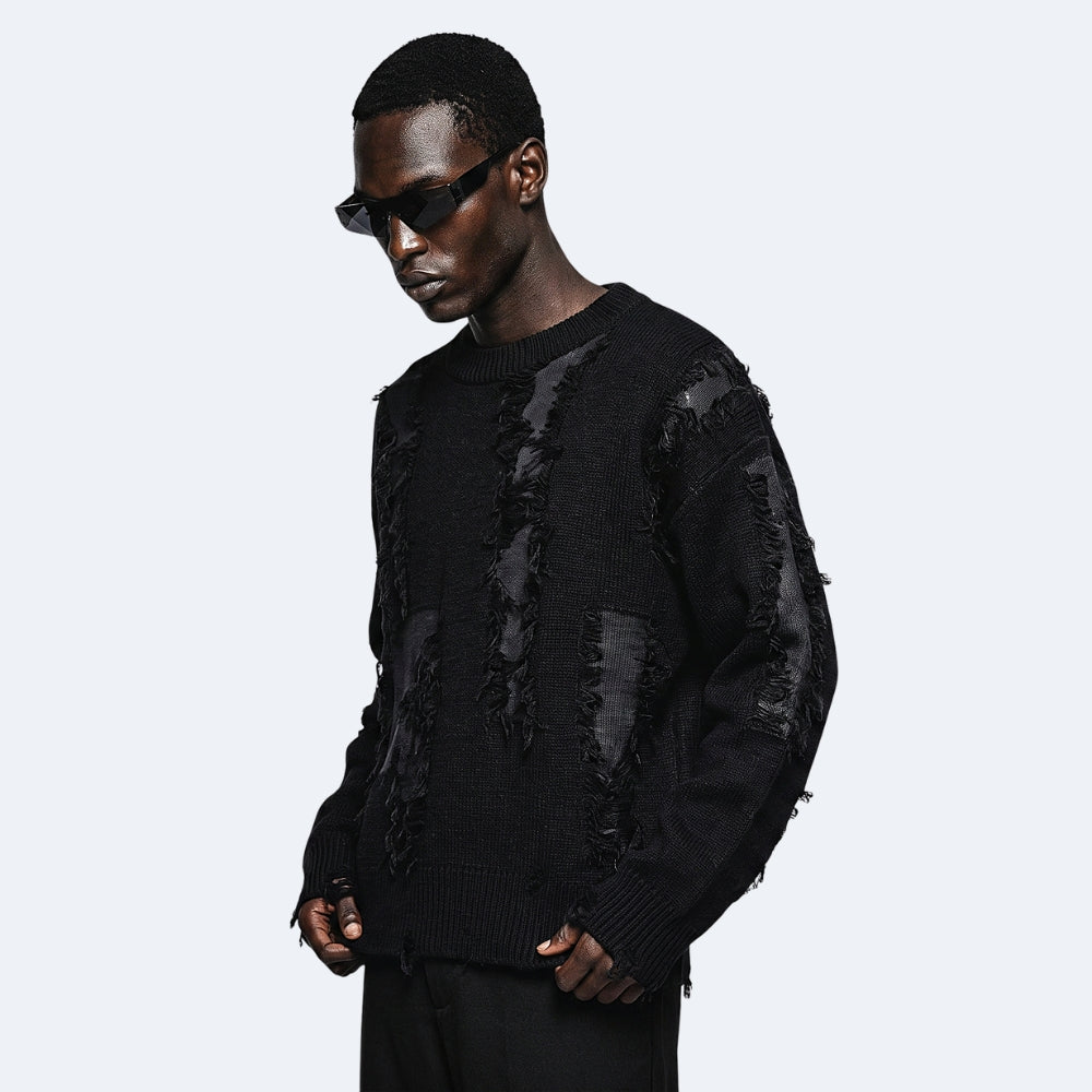 Black. A model wearing a black distressed knit sweater with raw frayed edges and sheer black panels, styled with black sunglasses.