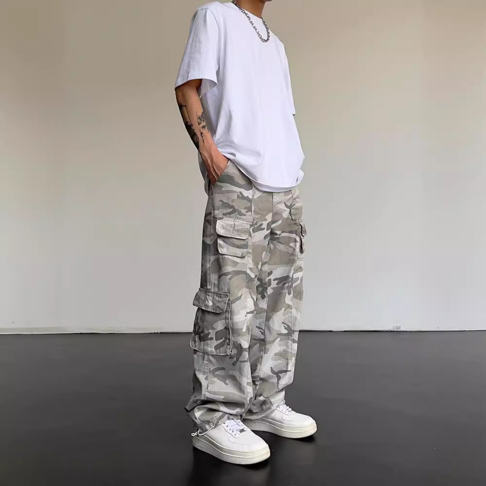 Person wearing camouflage pants and a white t-shirt against a plain background