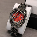 Elegant watch with red face and intricate metal band on a white stand