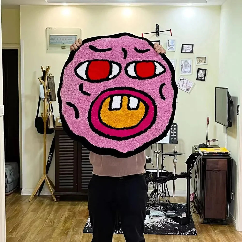 Person holding a large round pink rug with a face design in a room.
