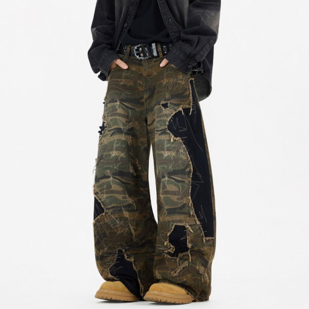 Camouflage pants with black patches worn by a person on a white background