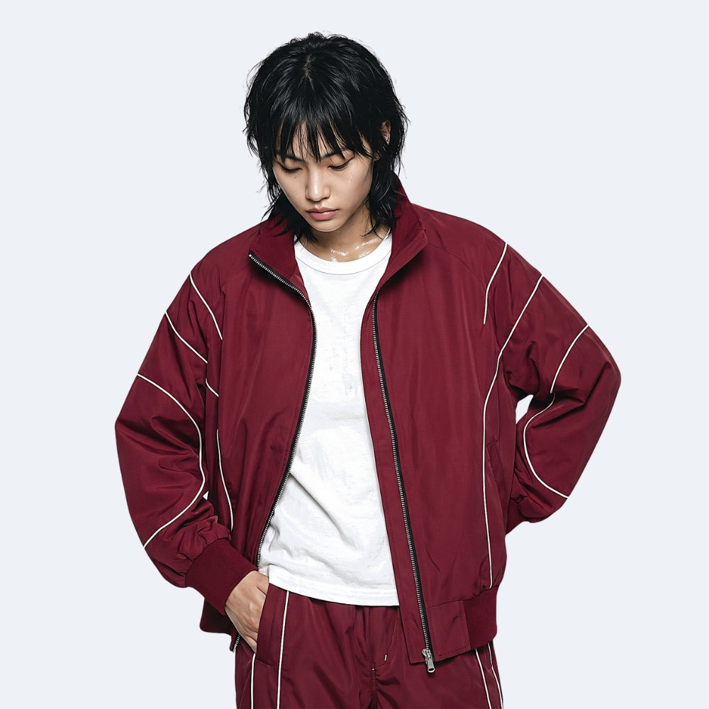 A model wearing a burgundy zip-up jacket with white contrast piping over a white t-shirt and matching burgundy pants, set against a plain light gray background.