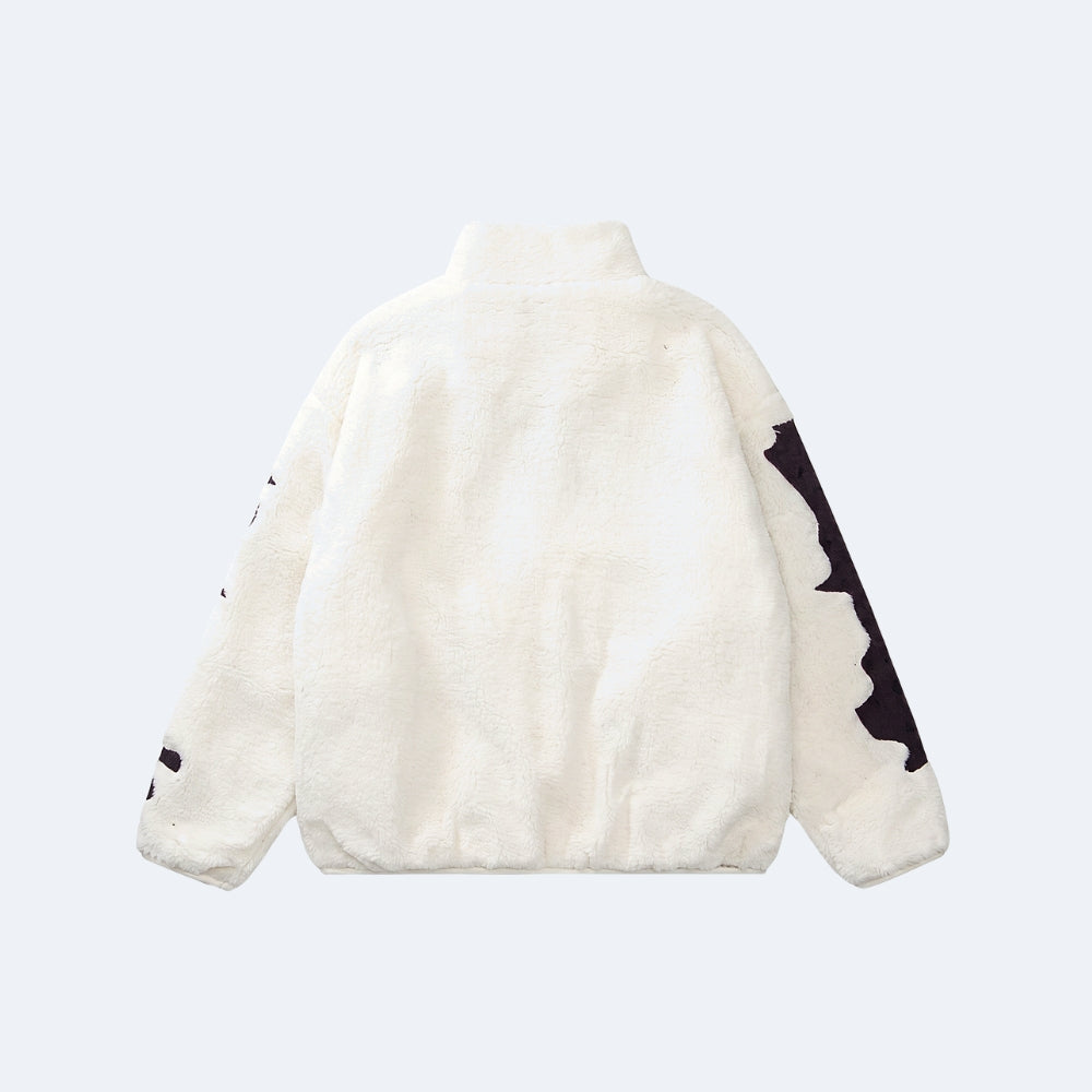 White. A cream-colored plush fleece jacket shown from the back, featuring black graphic patterns on the sleeves.