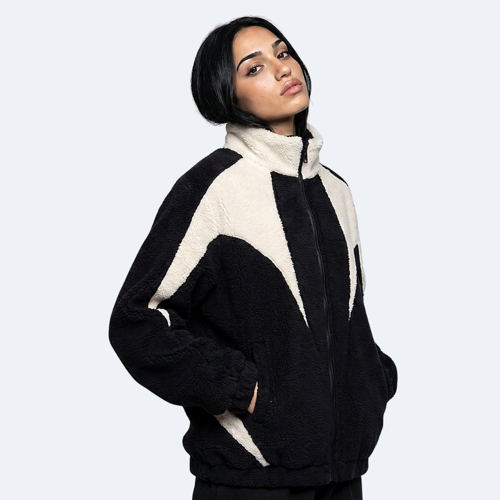 Black. A woman wearing a black and cream color-blocked sherpa fleece zip-up jacket.