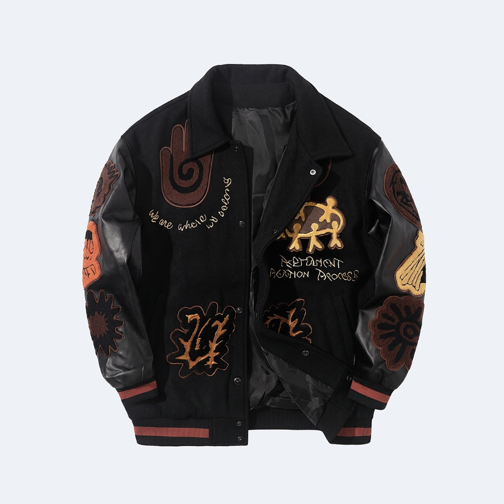 Black. A black varsity-style jacket with glossy faux leather sleeves, decorated with brown and gold gothic and occult-themed patches, embroidery, and text.