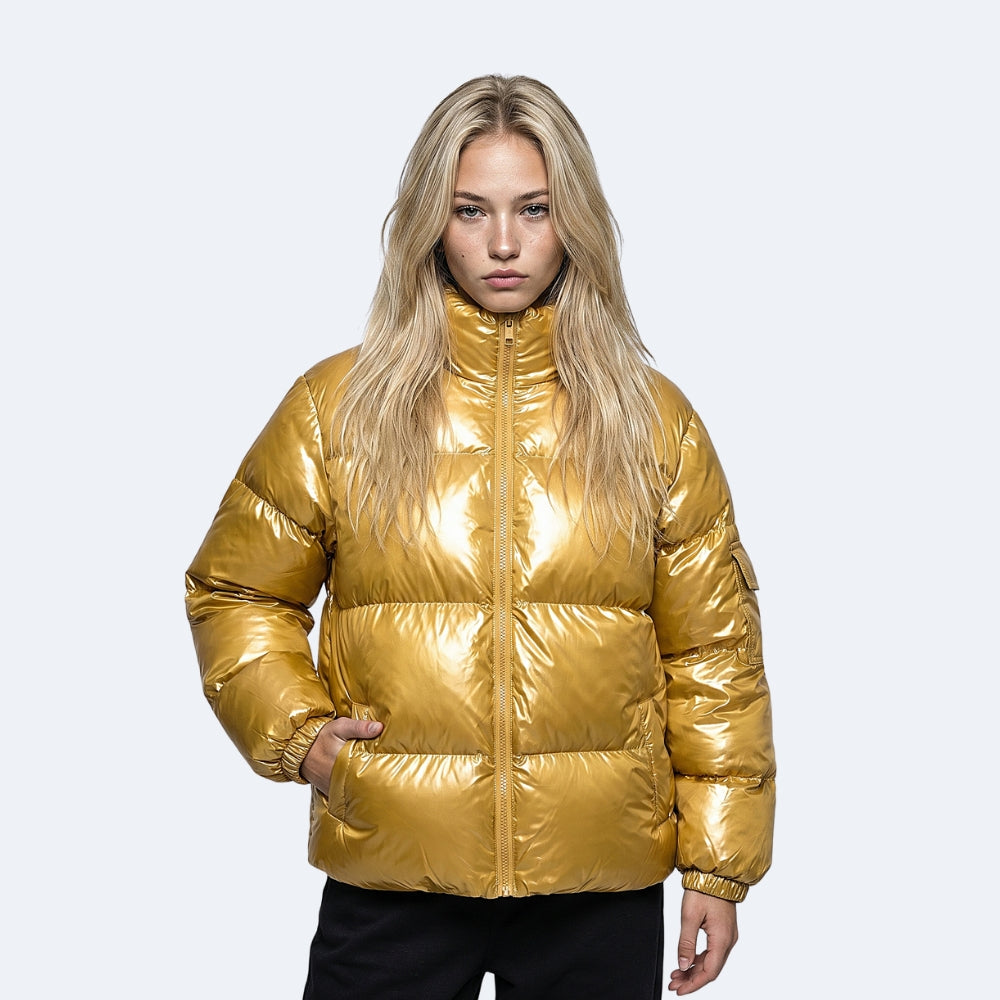 Gold. A blonde model wearing a shiny metallic gold puffer jacket with a high collar and front zipper, paired with black pants.
