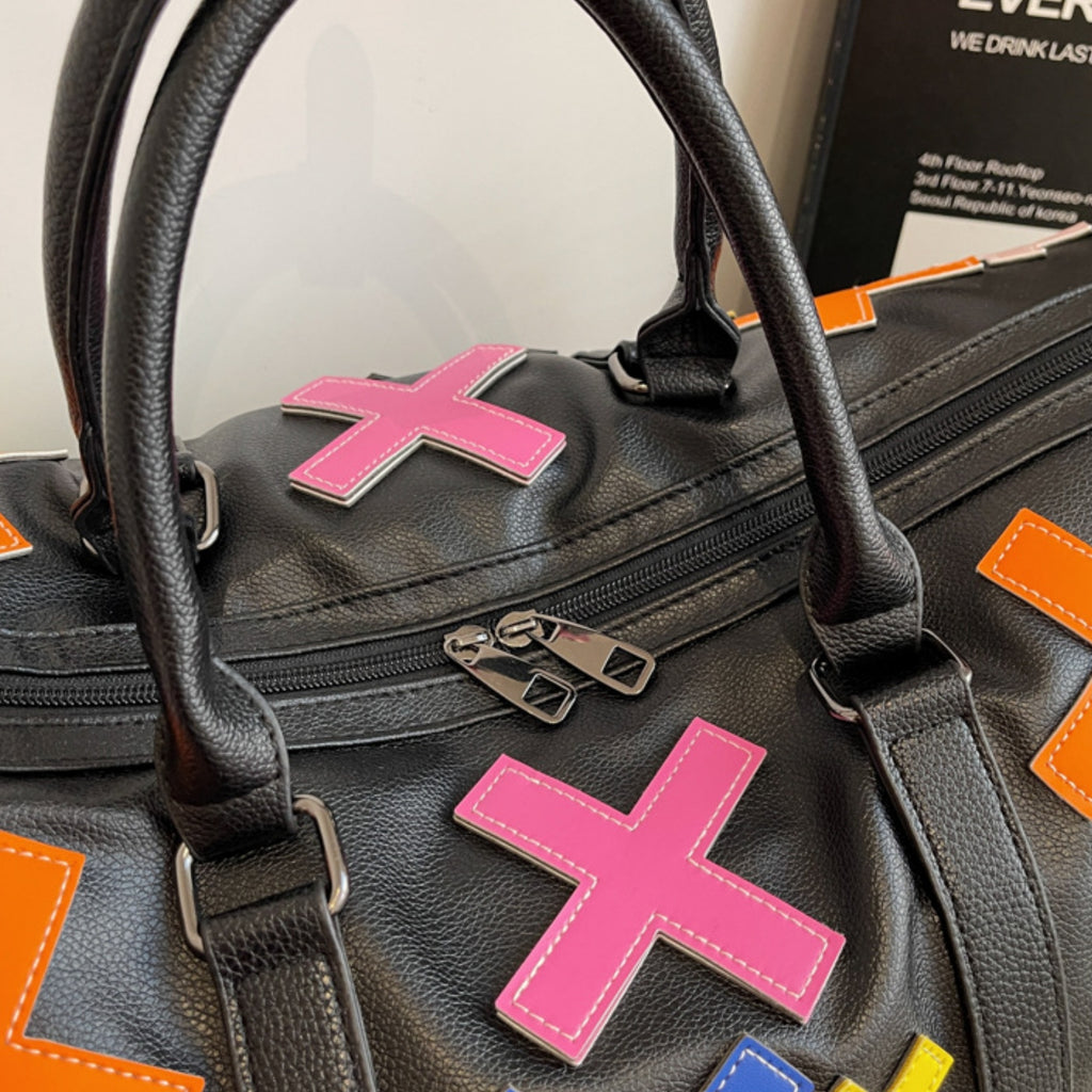 Black leather bag with pink 'X' and colorful accents on a blurred background