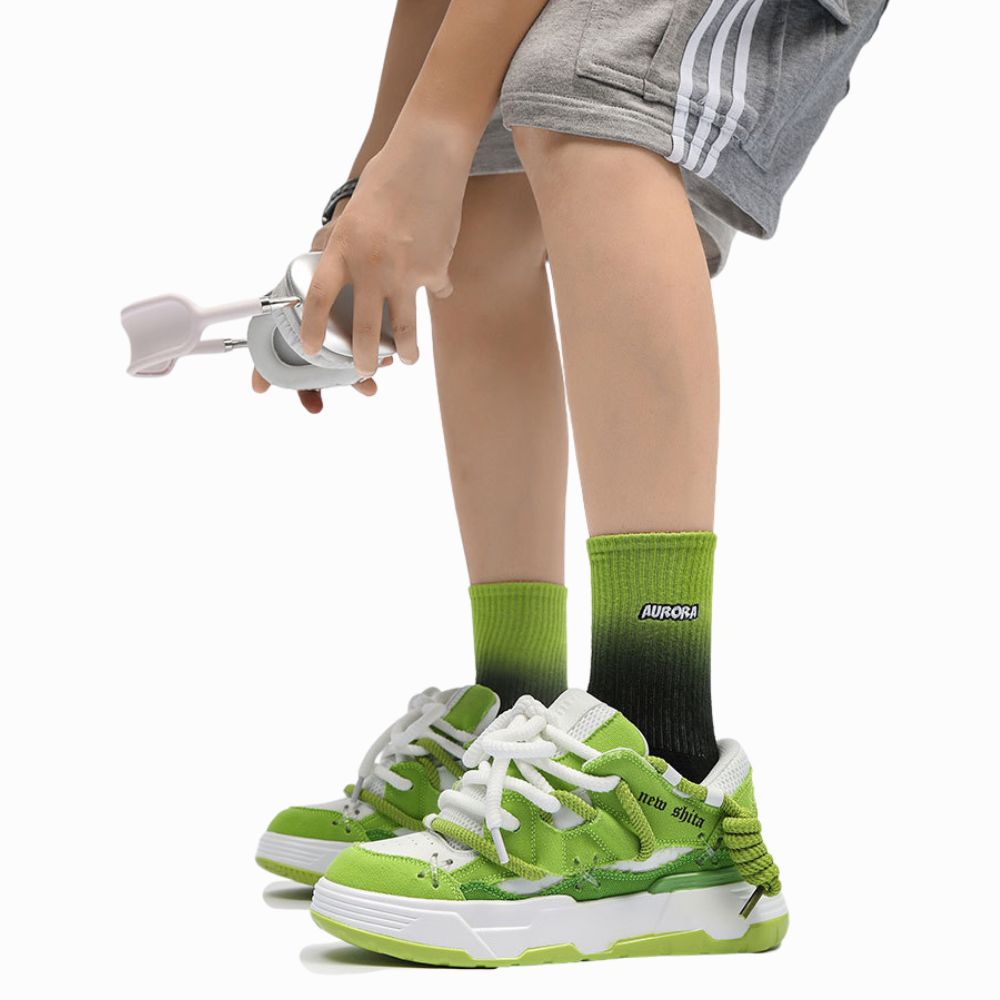 Person wearing green sneakers and gray shorts with white stripes, holding a phone.