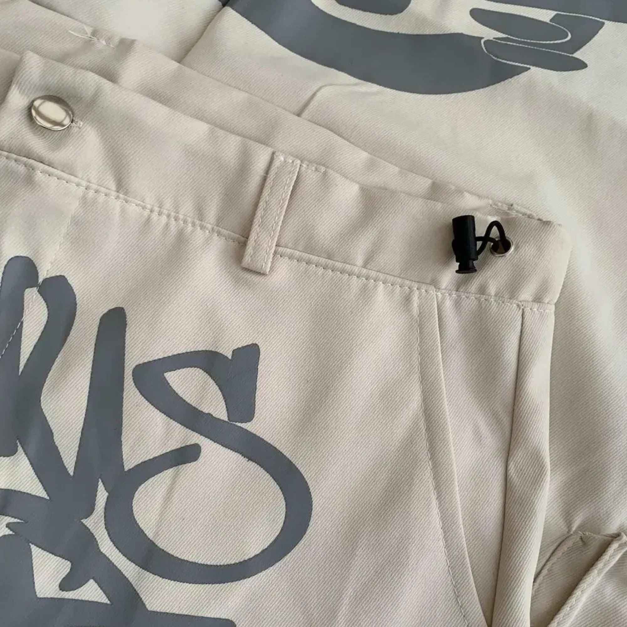 Close-up of beige pants with a brand logo on the back pocket.