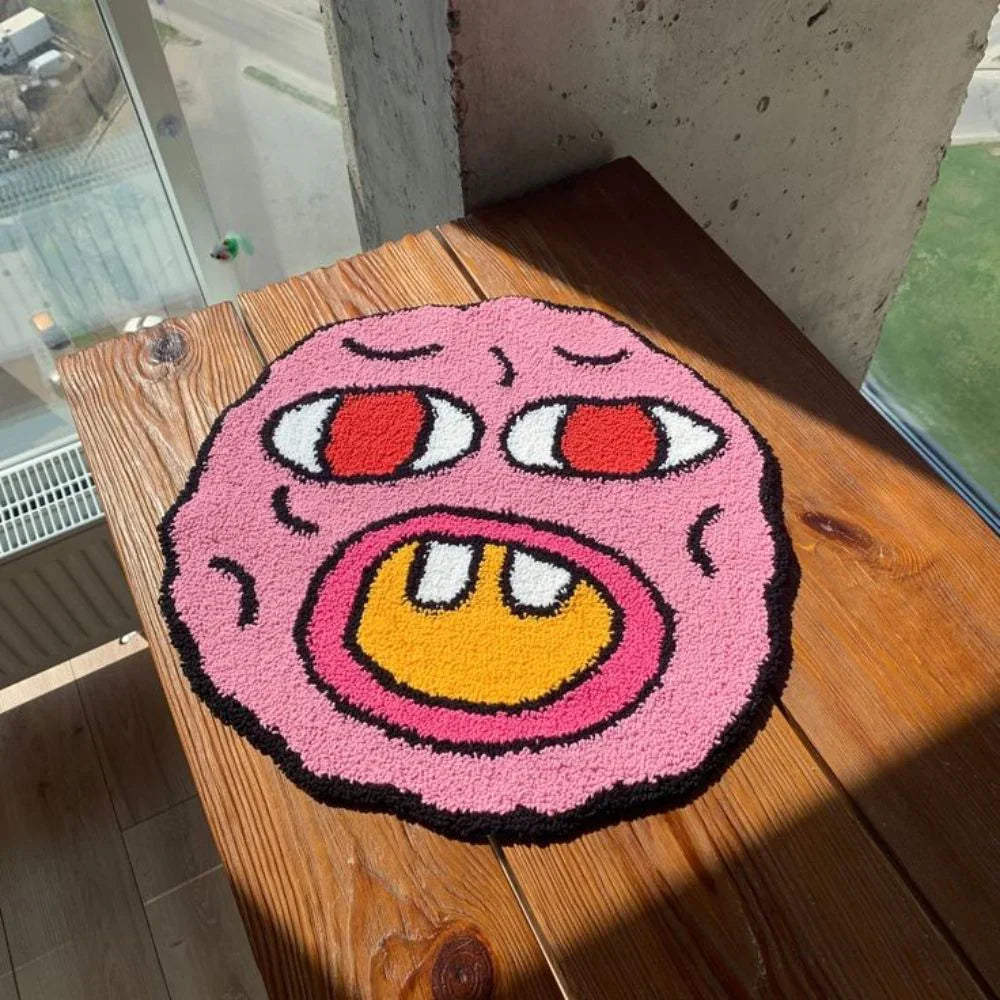 Pink cartoonish rug with a face on a wooden surface