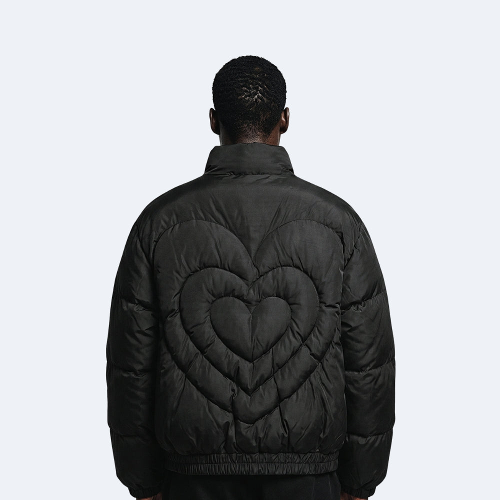 Black. A man viewed from behind wearing a black puffer jacket with a large quilted heart design on the back.