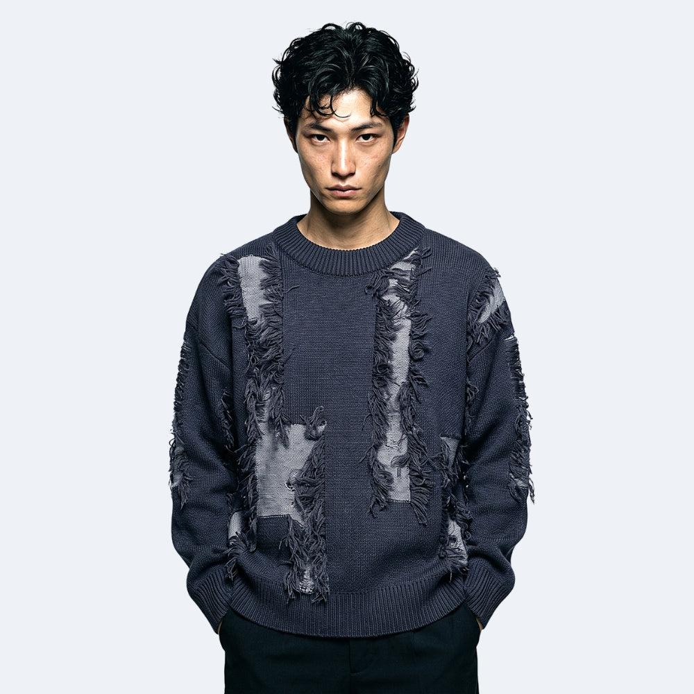 Dark Gray. A man wearing a dark charcoal gray distressed knit sweater with frayed details and black pants.