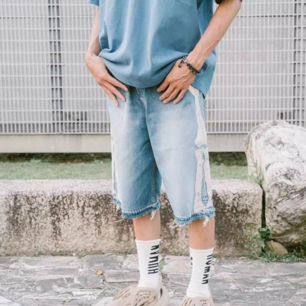 Person wearing a blue oversized shirt and light blue jeans with white socks outdoors.