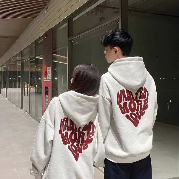 Two people wearing matching white hoodies with red text in a heart shape, walking together.