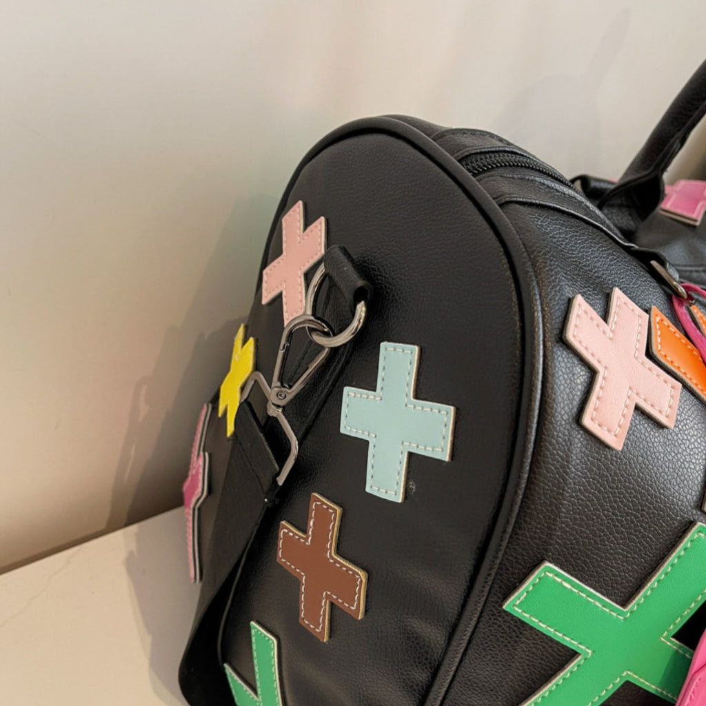 Black bag with colorful cross-shaped patches on a neutral background
