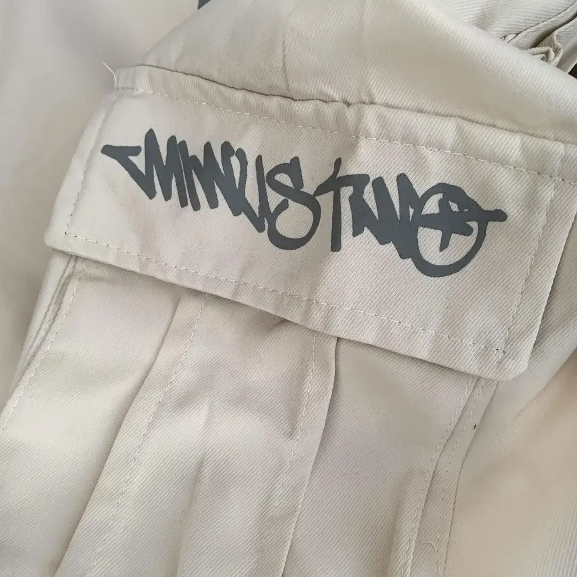 Close-up of beige pants with a black logo on the pocket