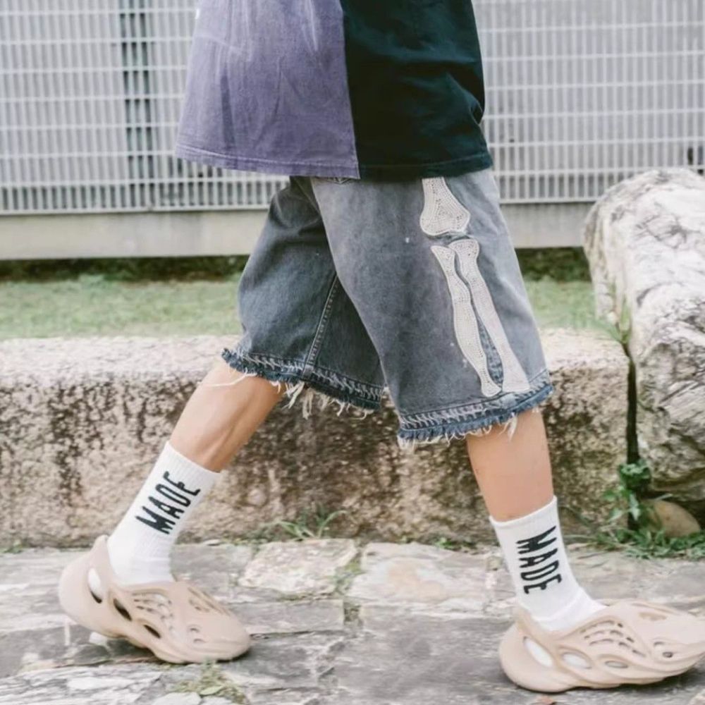 Person wearing denim shorts, white socks with text, and beige sandals on a stone path.