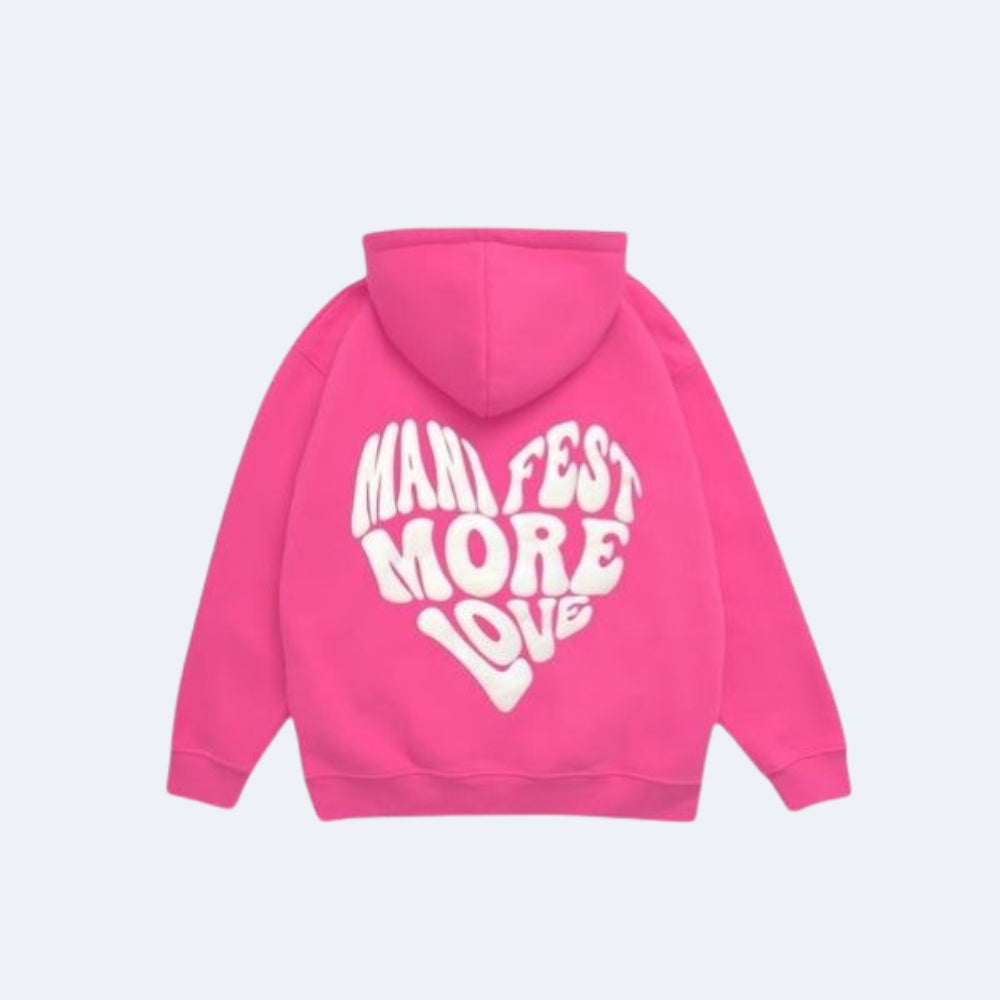 Pink. A bright pink hoodie shown from the back, featuring a large white retro-style graphic text that reads MANIFEST MORE LOVE across the back.