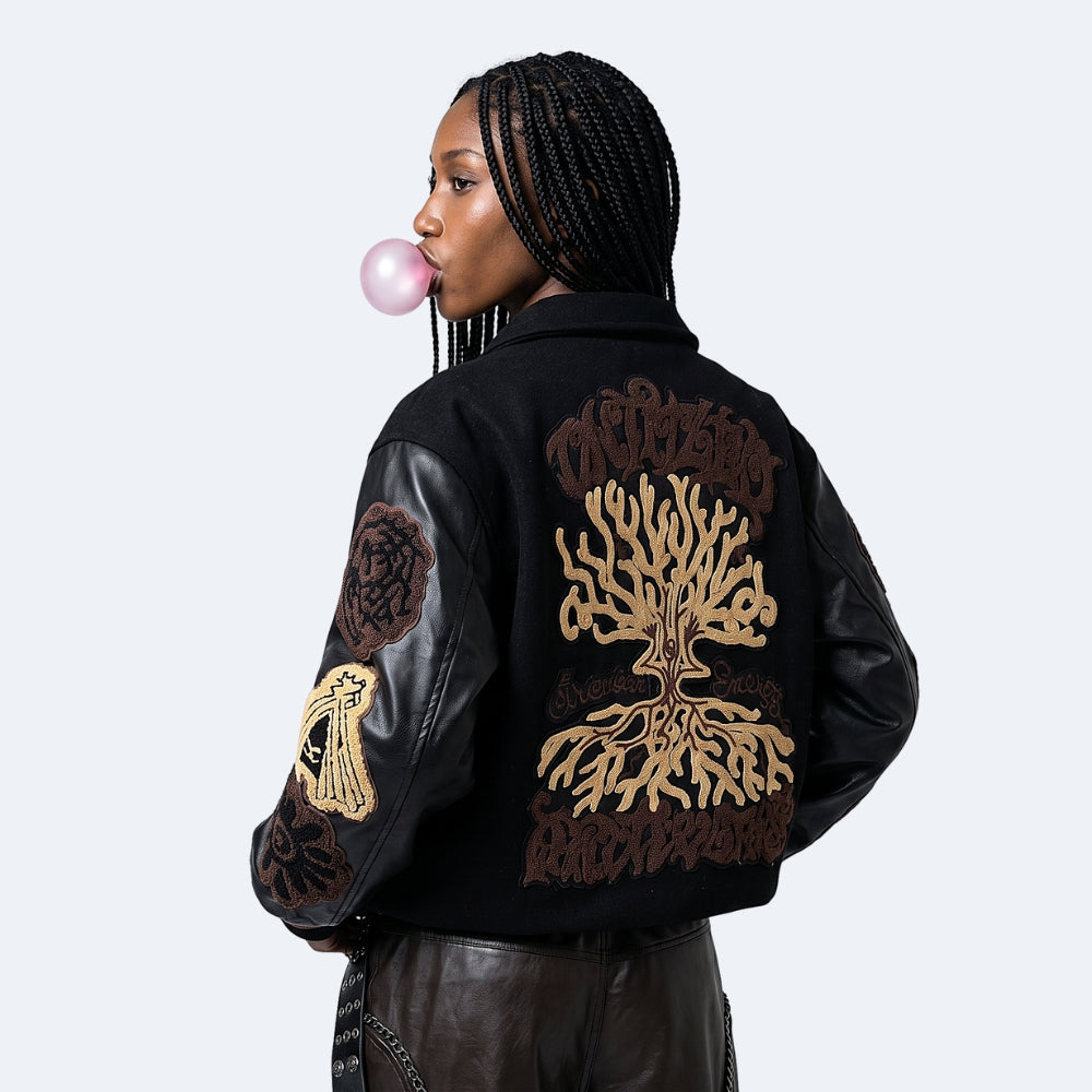 Black. A model from the back wearing a black leather and suede jacket with intricate brown and gold embroidered designs on the back and sleeves.